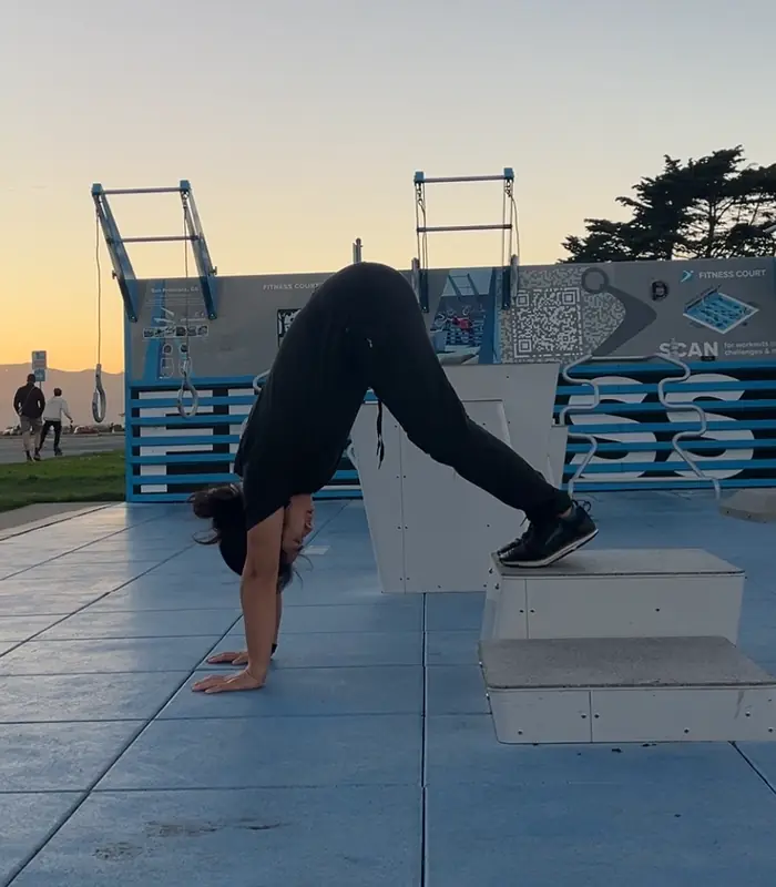 Selena Seto holding a pike push-up on the Marina Green fitness court at sunset