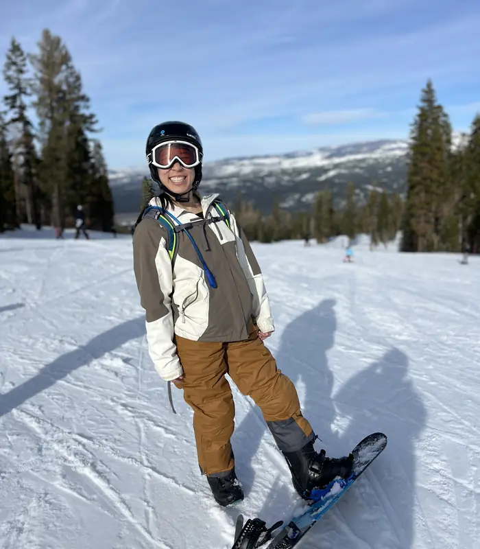 Selena Seto smiling on a snowboard on a sunny mountain slope