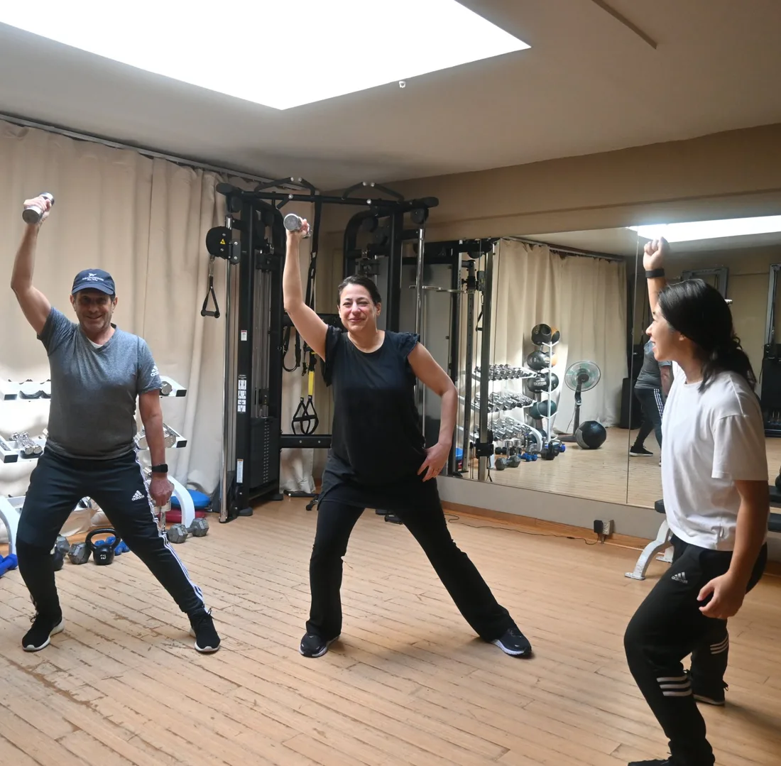 Selena leading two clients through a dumbbell lunge-and-reach exercise in the studio